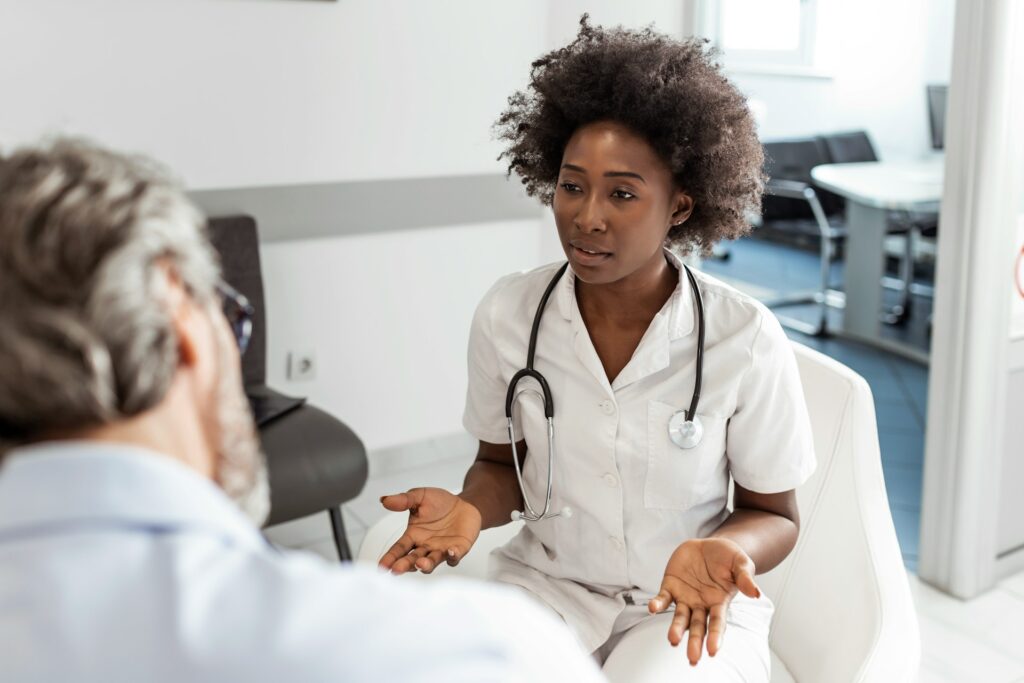 Doctor in white coat with stethoscope discussing with patient in a medical office, emphasizing communication during longer primary care visits.