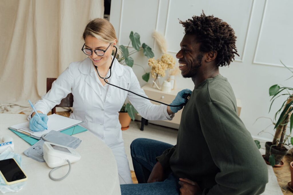 Female healthcare provider examining a smiling male patient with a stethoscope in a bright, welcoming clinic setting, emphasizing relationship-based primary care and same-day appointment accessibility.